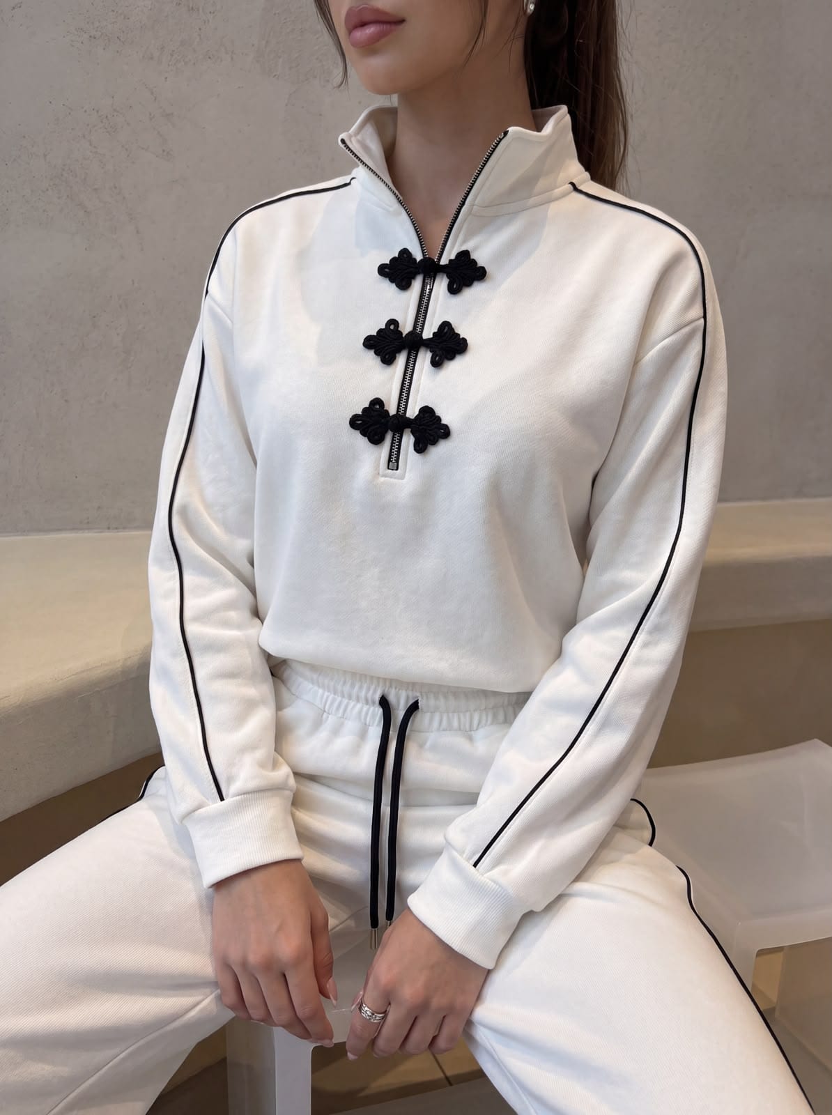 Black frog closures at the collar of a white set.
