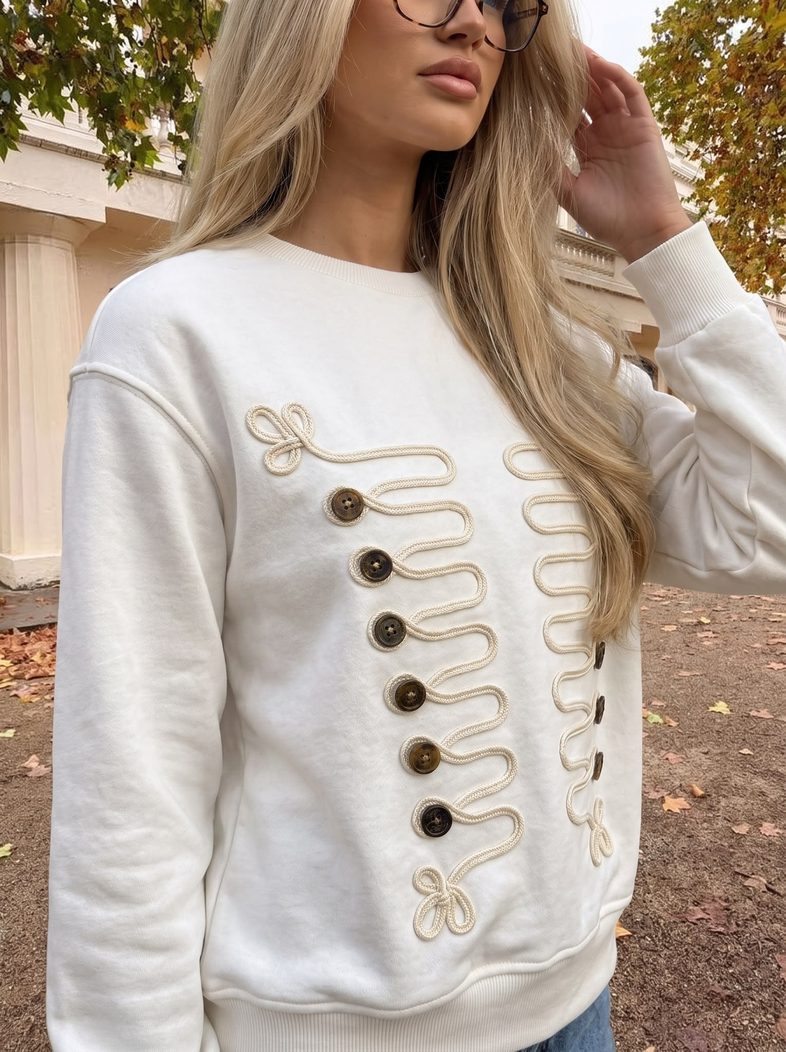 Close-up of braided cord trim and gold buttons on a white sweatshirt.
