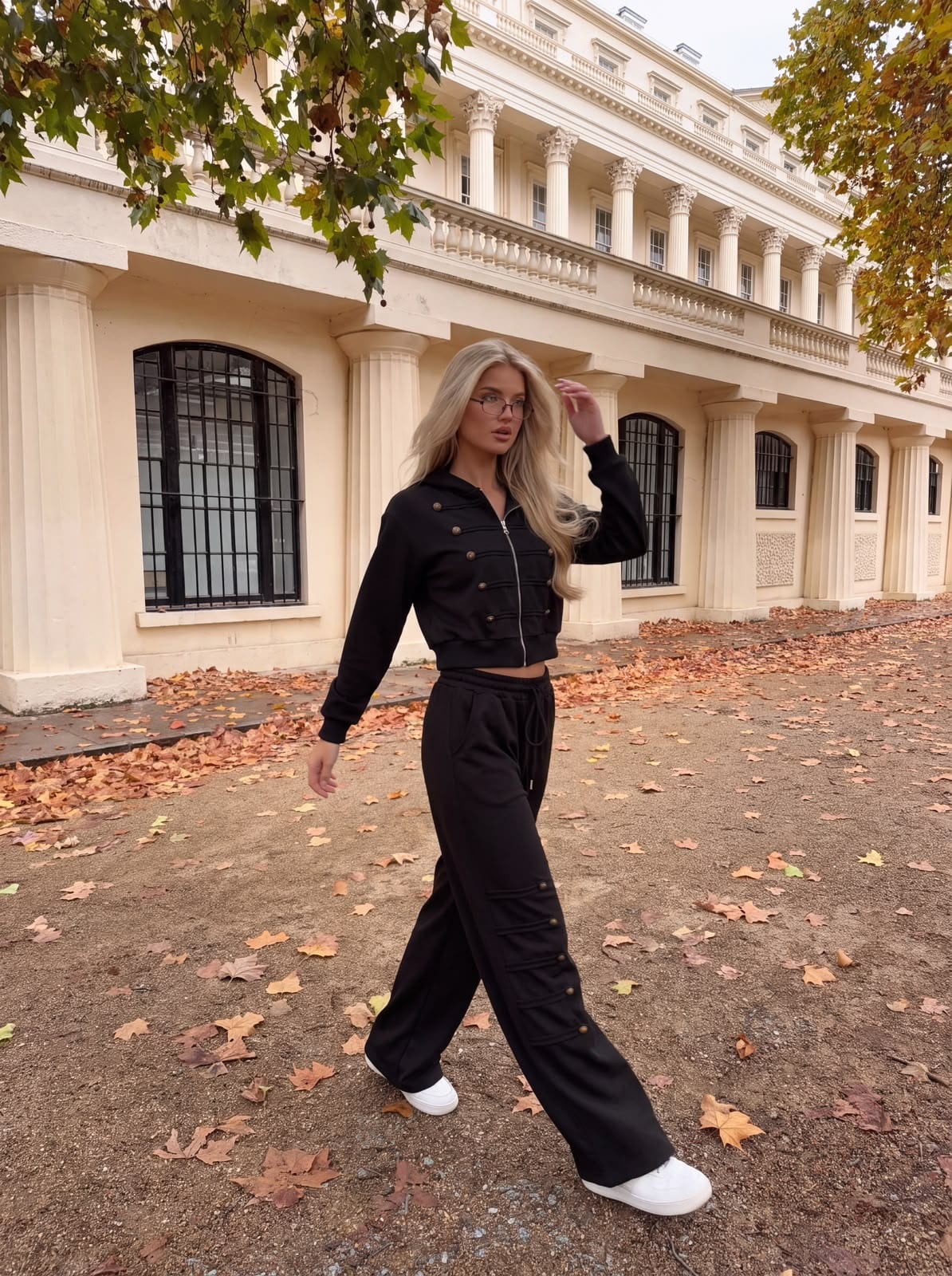 The same courtyard: model in a black button-detailed jacket and wide-leg trousers.