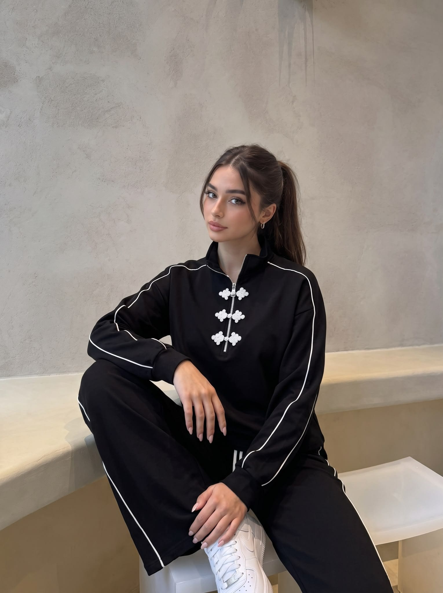 Model seated on a concrete bench in a black set with frog closures.