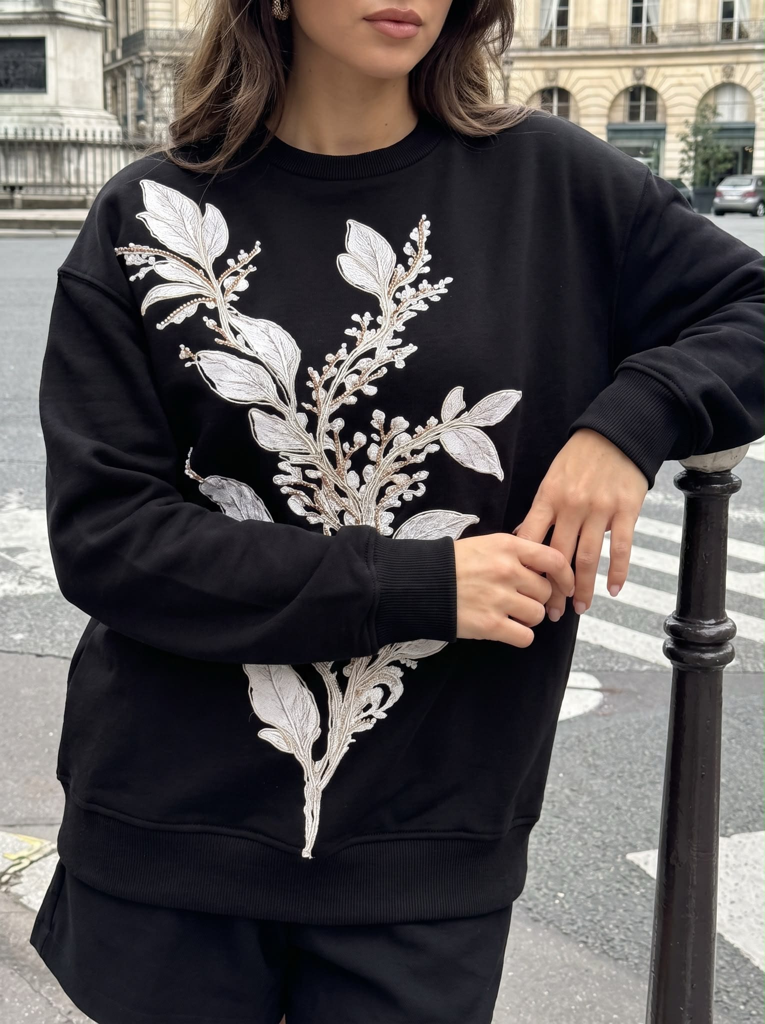 Silver and white leaf embellishment on a black sweatshirt.