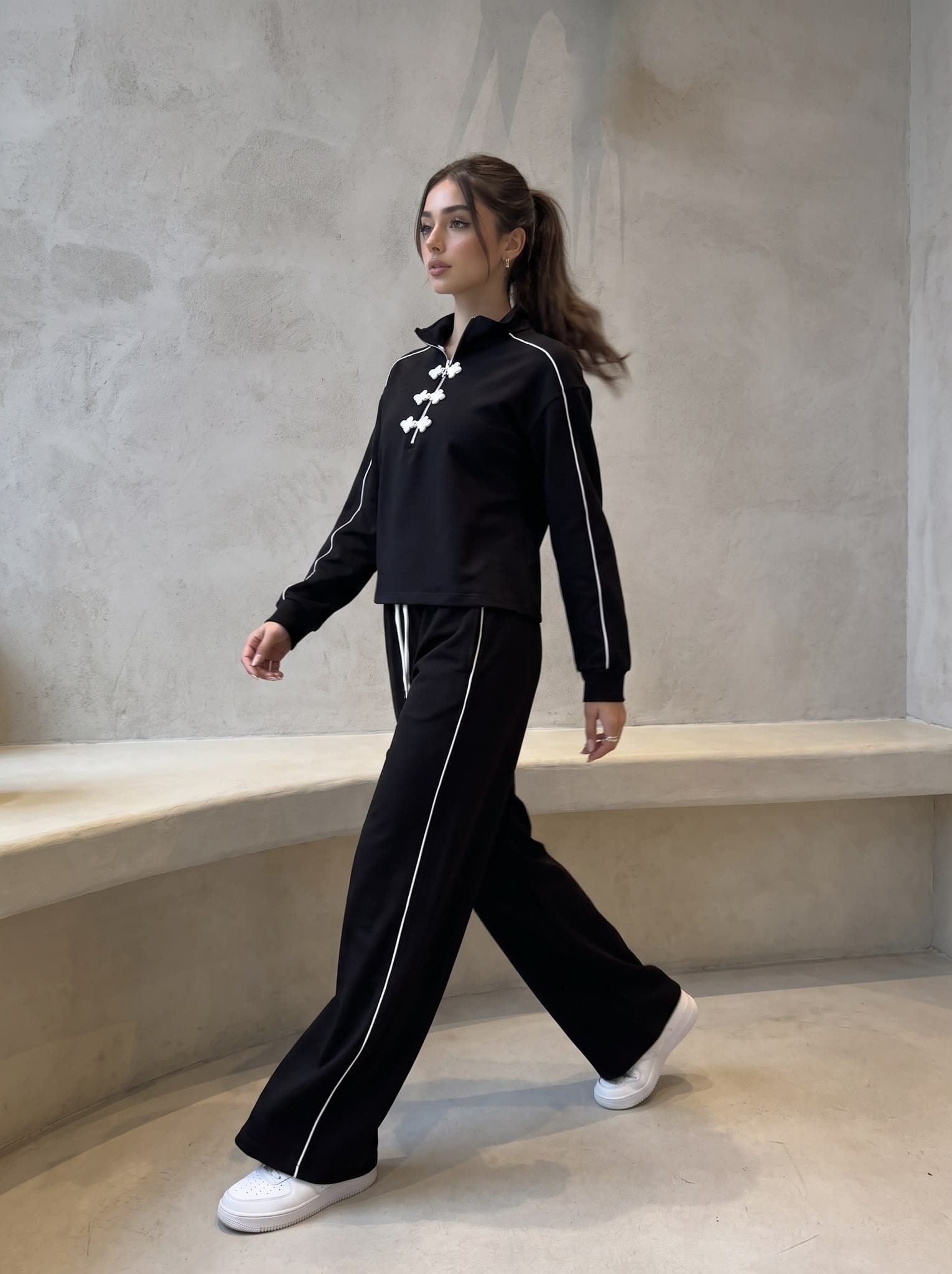 Model walking in a black tracksuit with frog closures and piping.