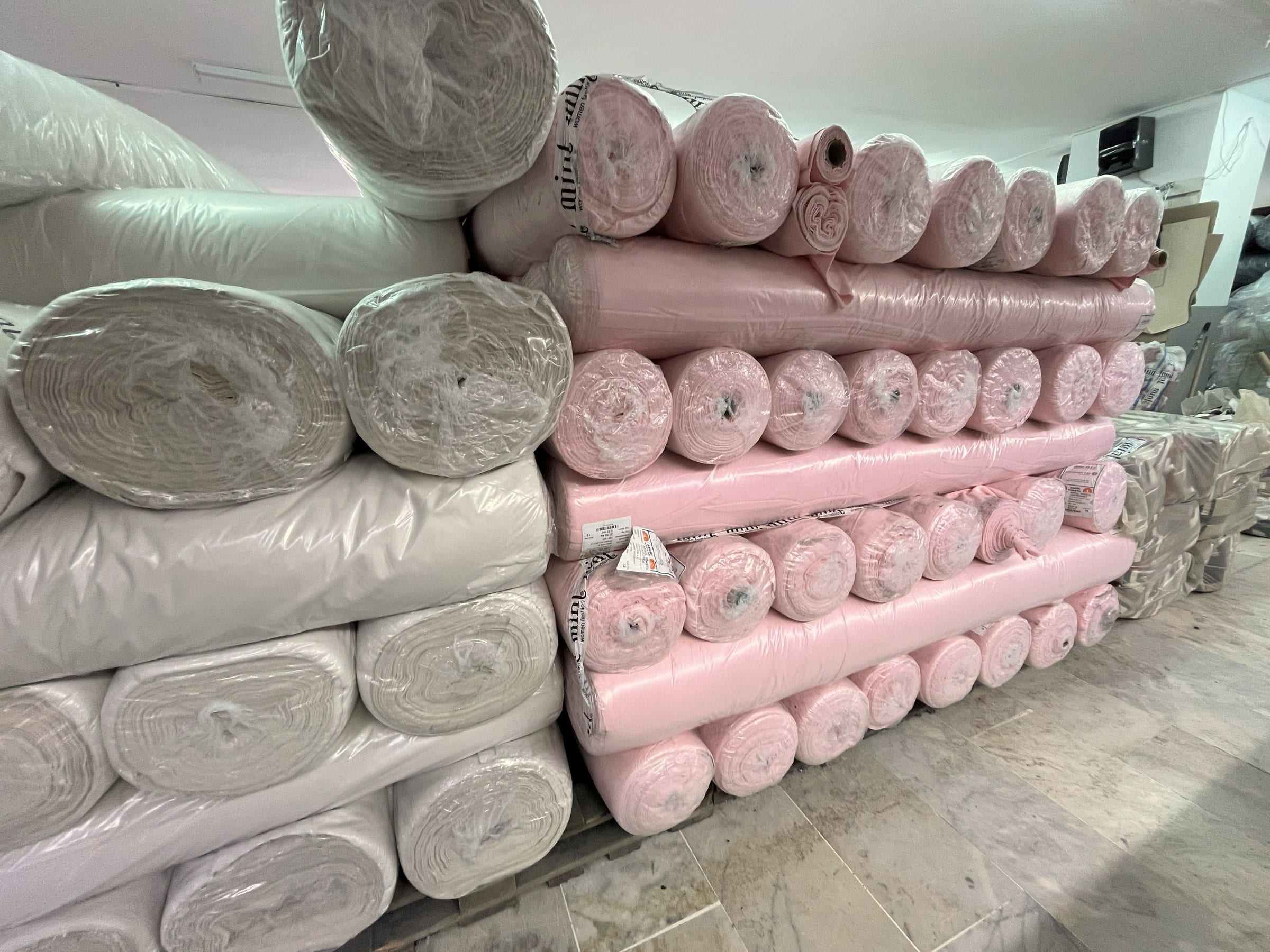 Pink and white fabric rolls stacked high in the cutting room.